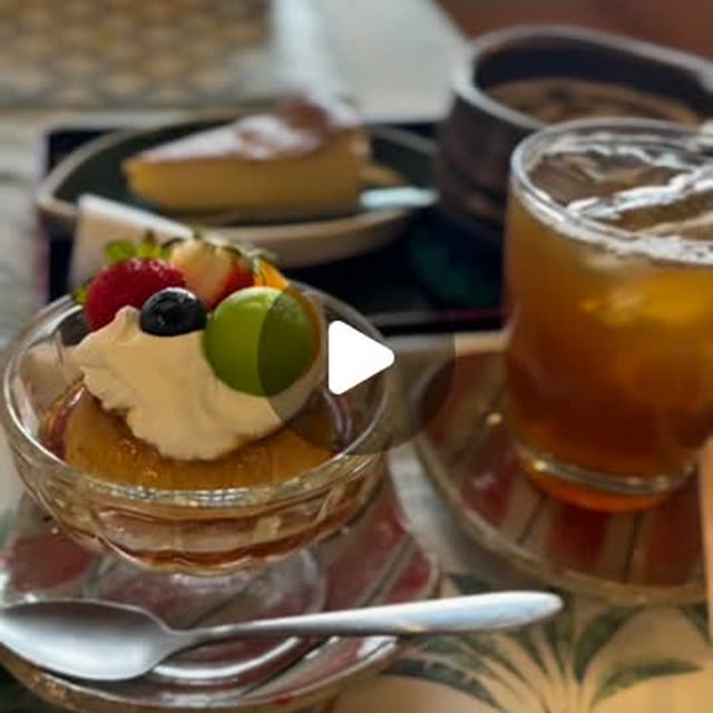 A fruit-topped dessert cup with whipped cream beside a slice of cheesecake and a tall glass of iced tea